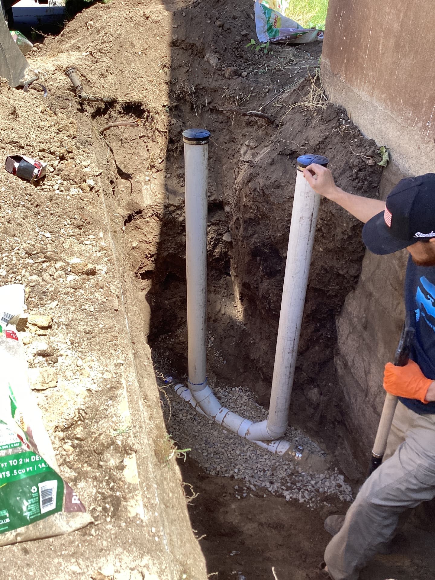 Open trench with new white PVC sewer line and cleanouts installed outside a Utah home